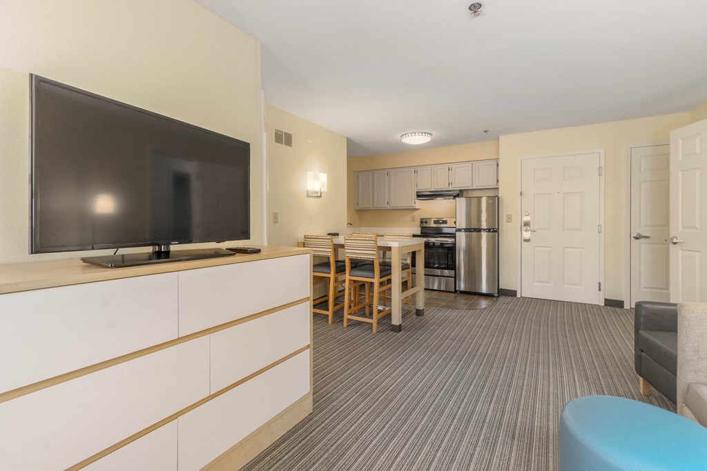 a living room with a television and a kitchen with a table and chairs